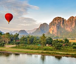 A hot air balloon flying at dawn over the river Nam Song at Vang Vieng, Laos with the scenic backdrop of the karst hill landscape surrounding the town